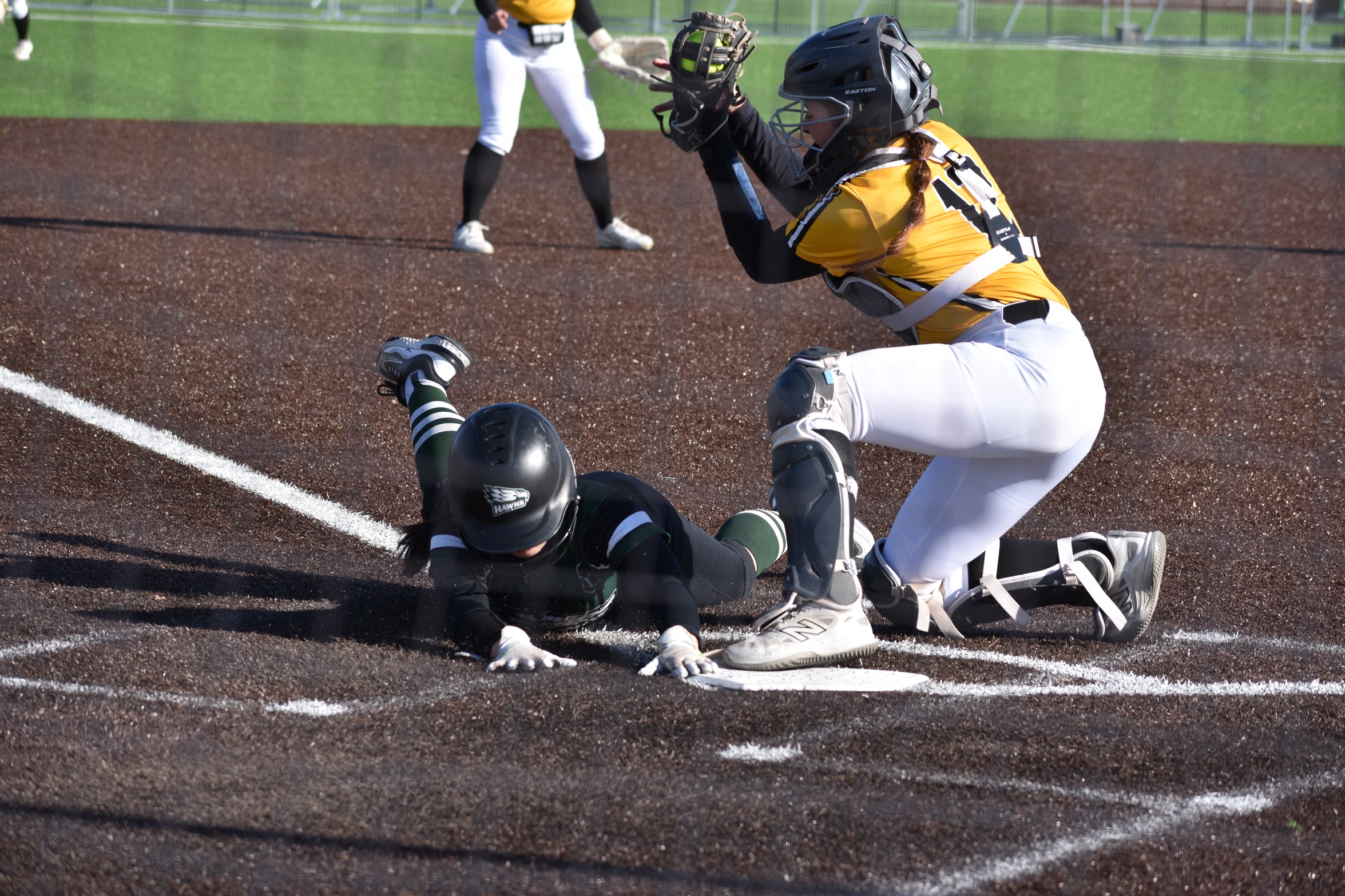 Hawks player slides under the tag at home plate.